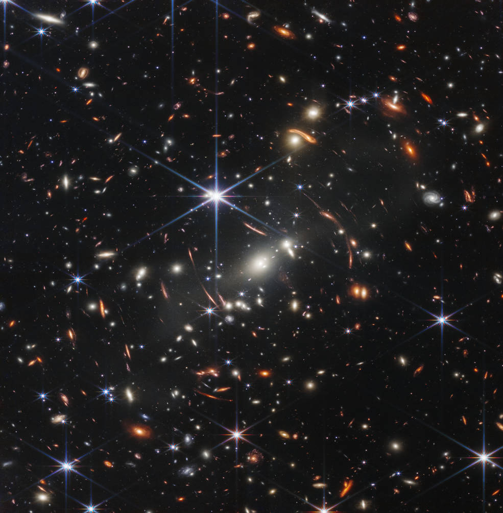 Image of a galaxy cluster by the James Webb Space Telescope shows a black background dotted with dozen of stars and shapes of galaxies