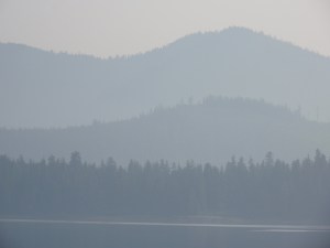 Photograph of foggy tree-covered hills layered in front of each other with water in the foreground