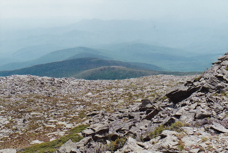 View from mountain with large boulders in foreground and misty ridges leading to horizon