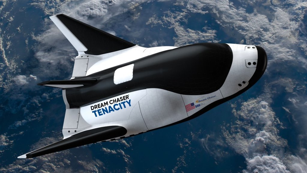 Artist representation of a small cargo space plane with Earth and clouds below. Black and white with wings. Name on the side: Dream Chaser Tenacity. Small American flag on the side.