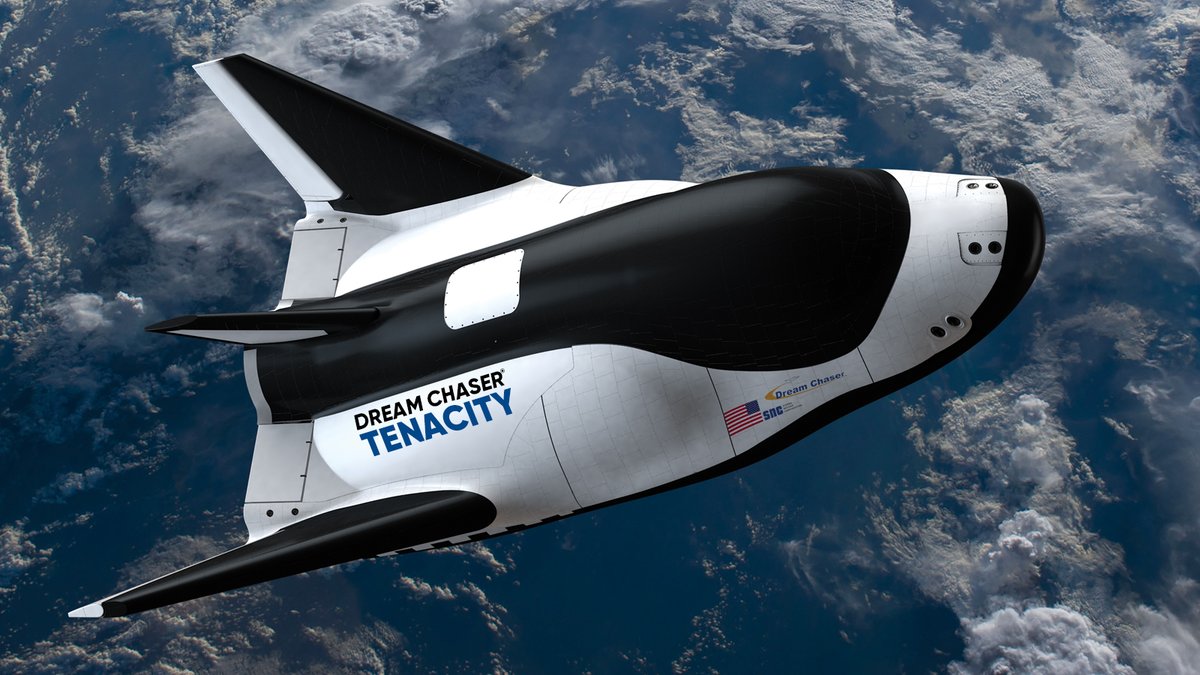 Artist representation of a small cargo space plane with Earth and clouds below. Black and white with wings. Name on the side: Dream Chaser Tenacity. Small American flag on the side.
